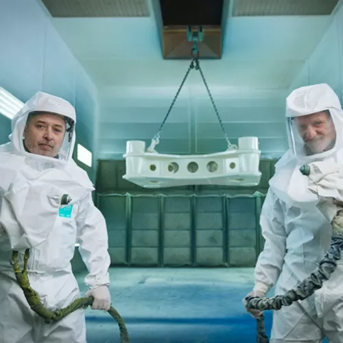 Twee werknemers van Valtech dragen een coverall en staan in een spuitcabine. 