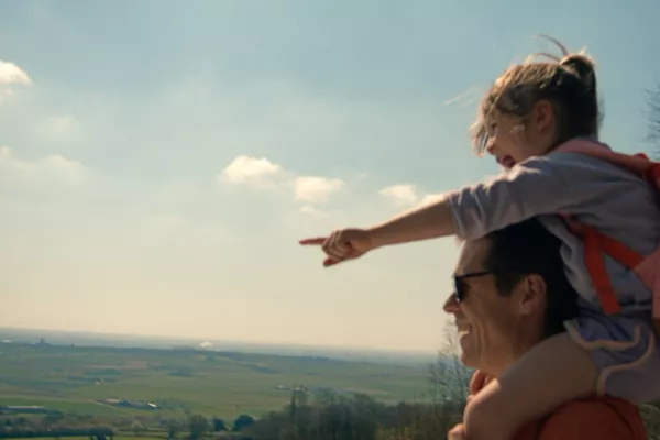 Man met dochter op schouders bij mooi uitzicht.