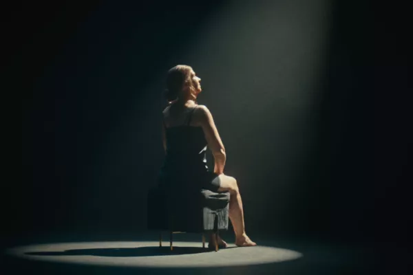 Een vrouw vol littekens op een stoel onder een spotlight.