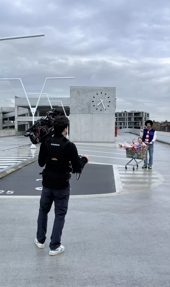 Een meisje zit in een winkelkar vol met Croky chips. De cameraman staat klaar om haar te filmen.