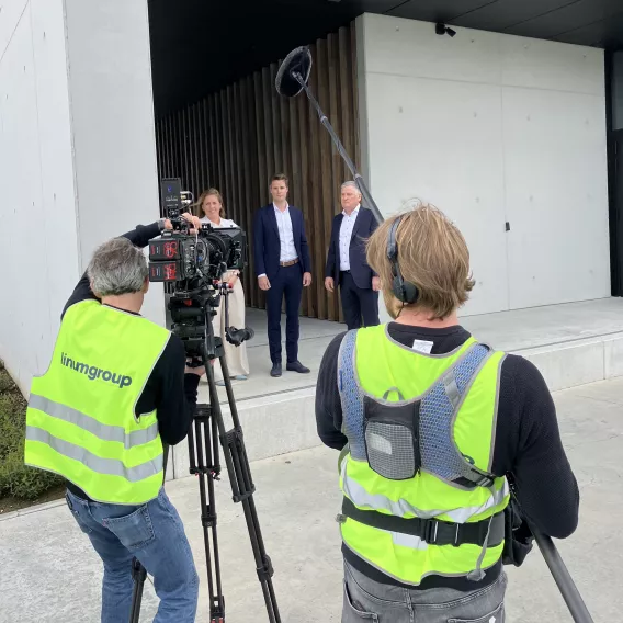 De CEO en zijn zoon en dochter staan voor de ingang van Linum en worden gefilmd.