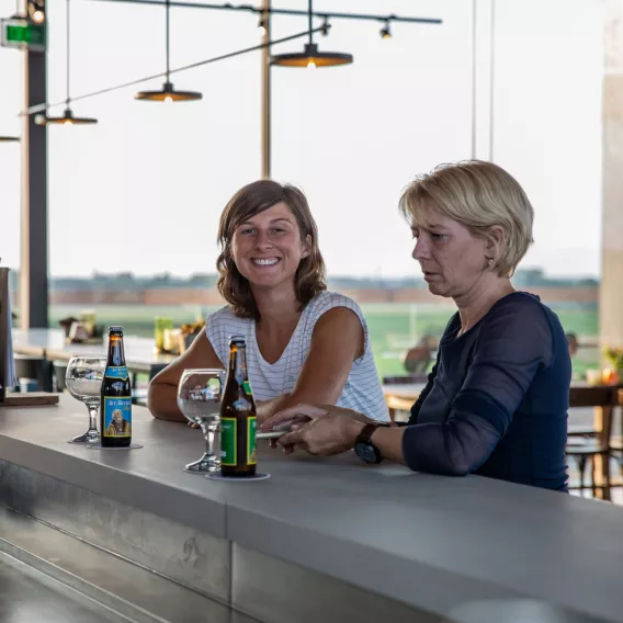 Twee dames genieten van een biertje aan een bar.