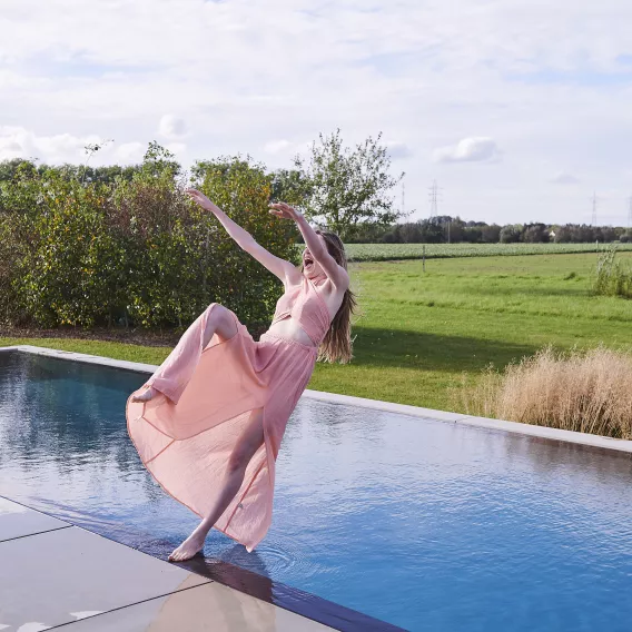 Een jonge vrouw laat zich vanop de rand van een zwembad in het water vallen.
